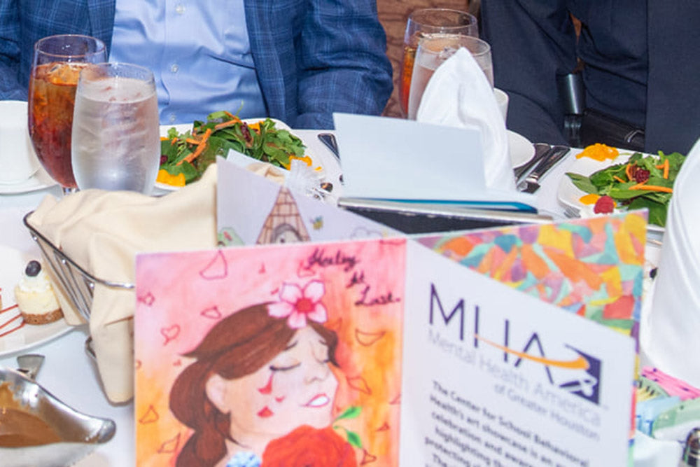 The top half of the centerpiece is visiable on the banquet table surrounded by drink glasses, salads, desserts and napkins. Two people sit at the far side of the table.