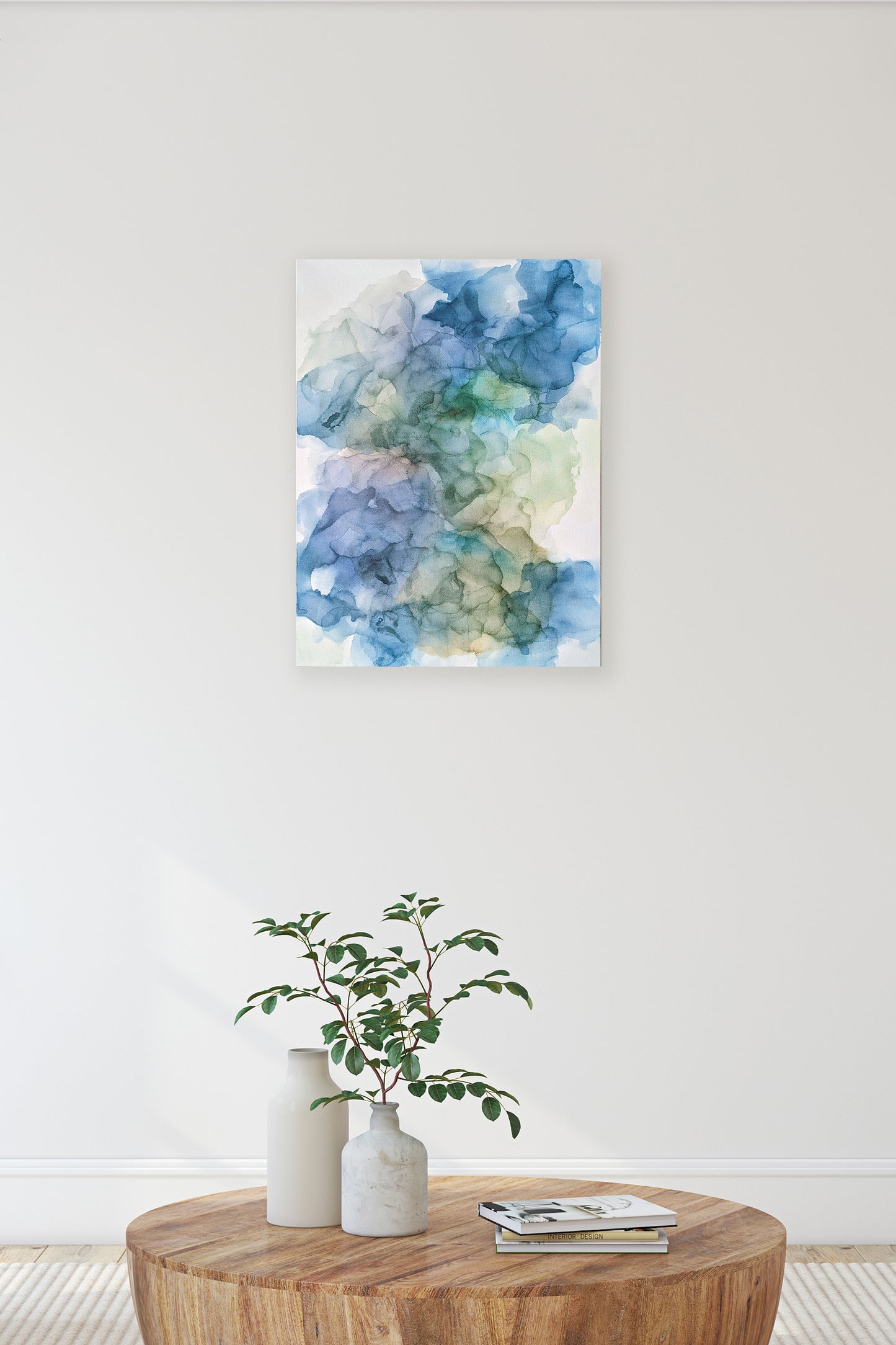 Digital mockup of Moon Water hung on a white wall in a living room. A wooden coffee table with ceramic vases, greens, and a stack of books is in the foreground.
