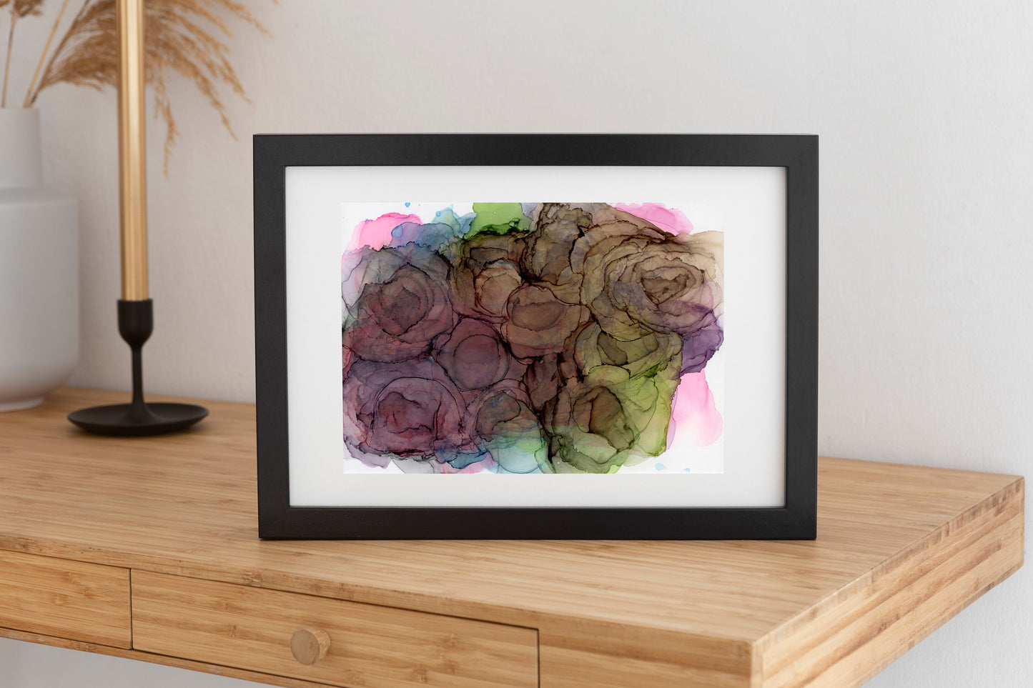 Digitgal mockup of Mysteries Waiting to be Explored framed in black propped up on a wooden console table. A gold candlestick in a black holder and a white vase sit against a white wall in the background.