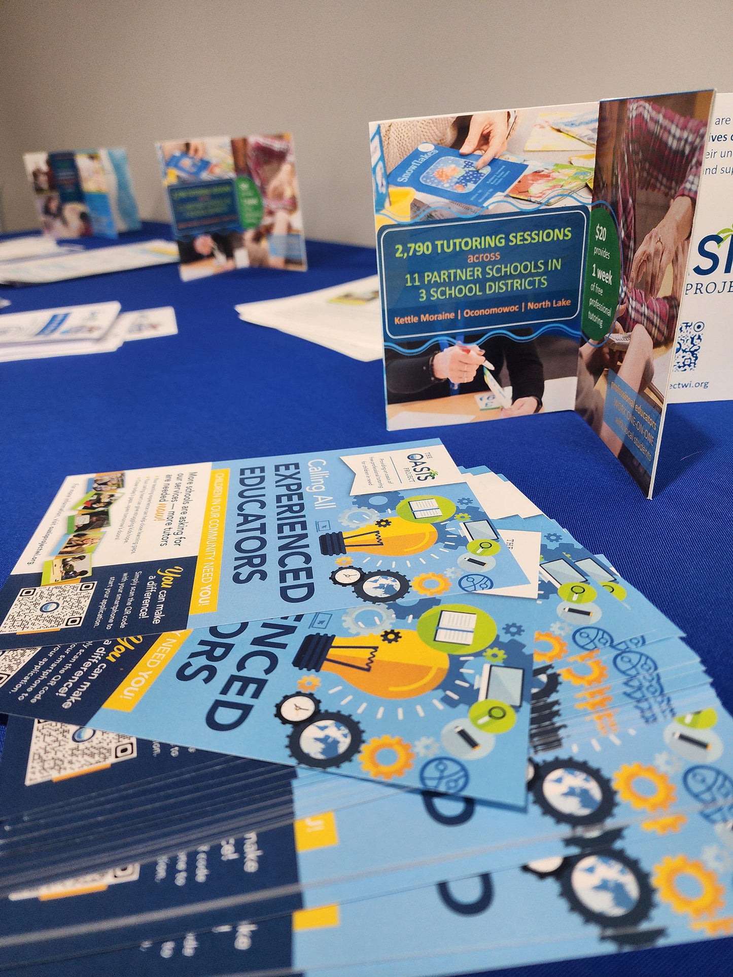 Three centerpieces sit on a blue tablecloth information table amidst brochures and handouts.