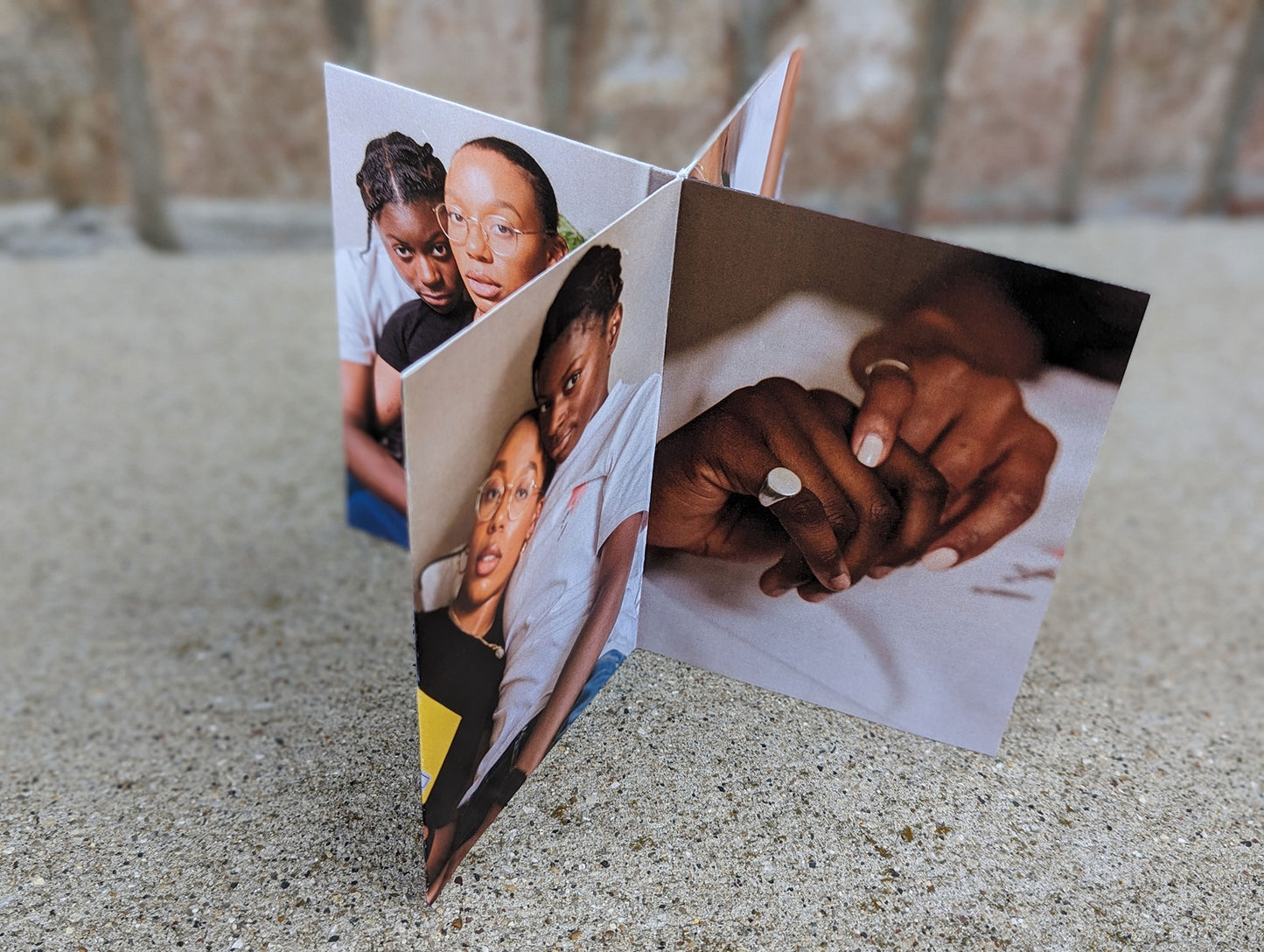 Centerpiece standing on a concrete surface with brick in the background of an LGBTQ+ couple smiling at the camera and showing off their rings.