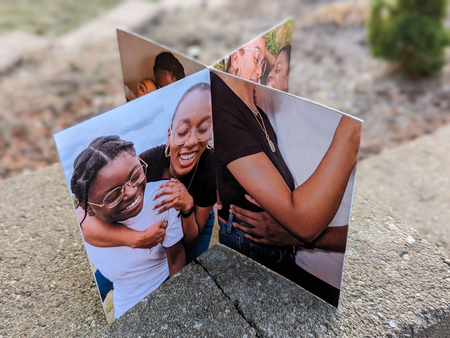 Centerpiece standing on a concrete surface showing engagement photos of an LGBTQ+ couple hugging laying on the grass laughing with each other.