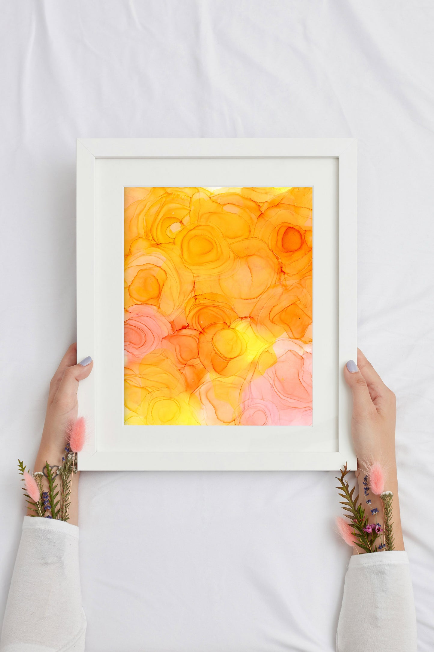 Digital mockup of two hands holding Open to Growth framed in white over a white comforter.