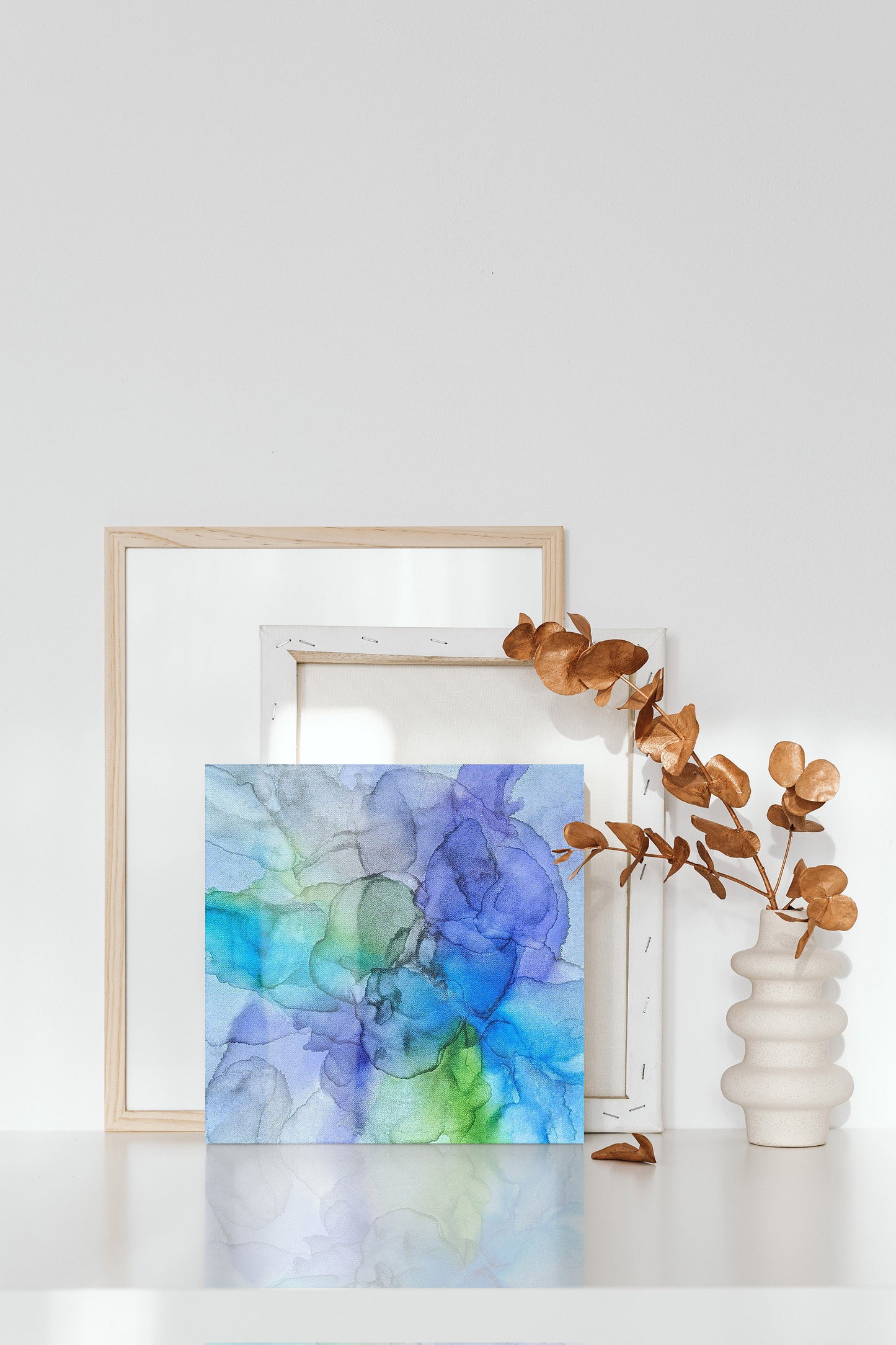 Digital mockup of Perseverance leaning against another canvas and frame with a ceramic vase and copper leaves next to it.