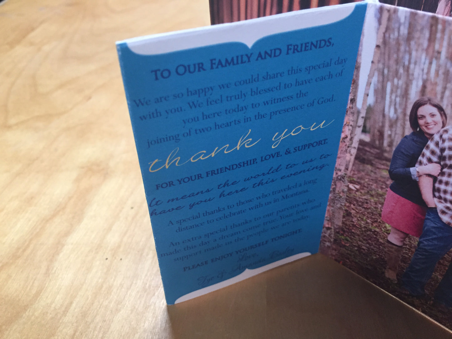 Centerpiece standing on a wooden table. The panels show a couple in the woods smiling at the camera and the thank you note to their family and friends.