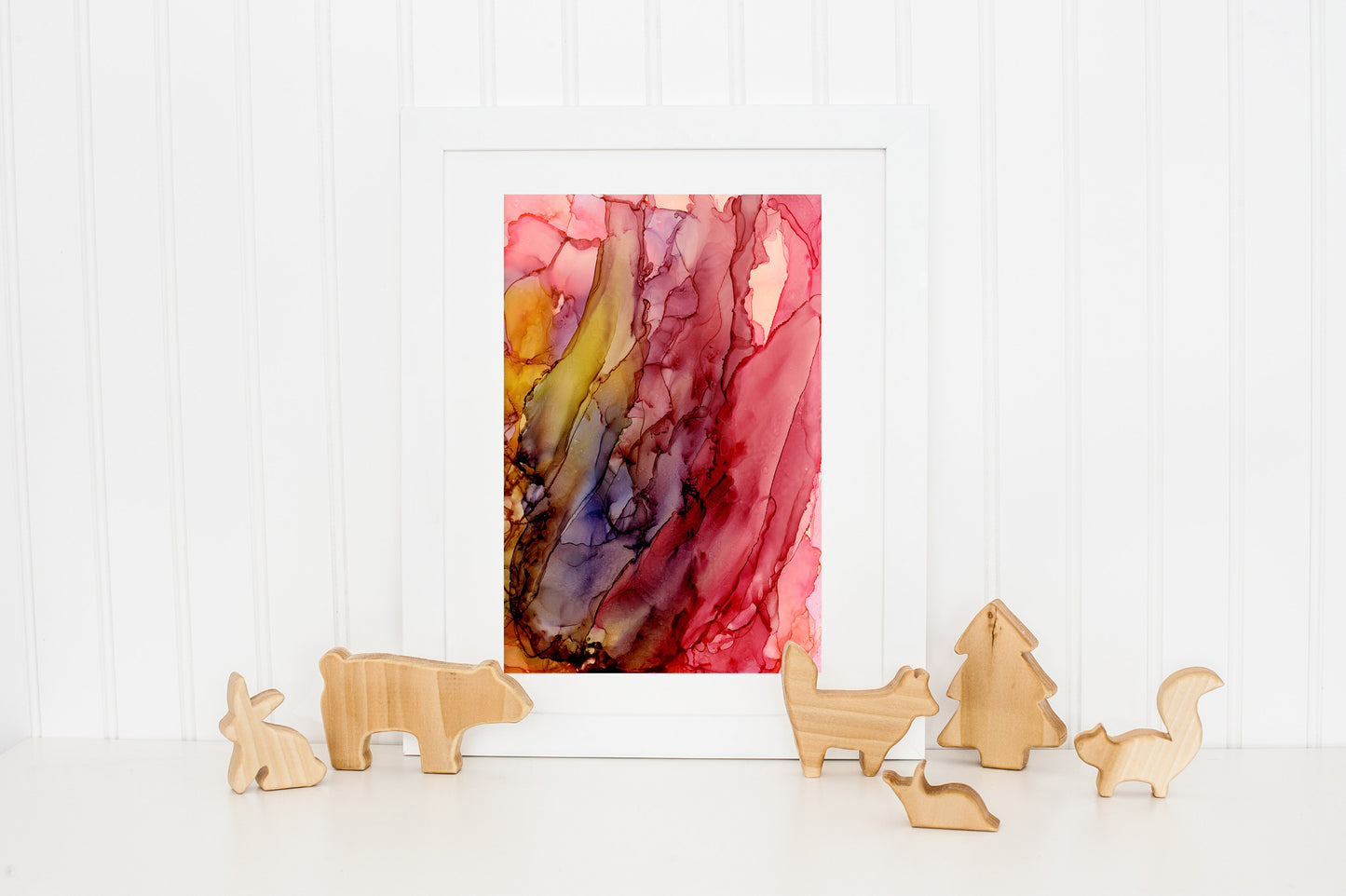 Digital mockup of Renewed Commitment framed in white standing on a white countertop and leaning against a white beadboard wall. There are wooden animal and tree cutouts standing at the base of the piece.