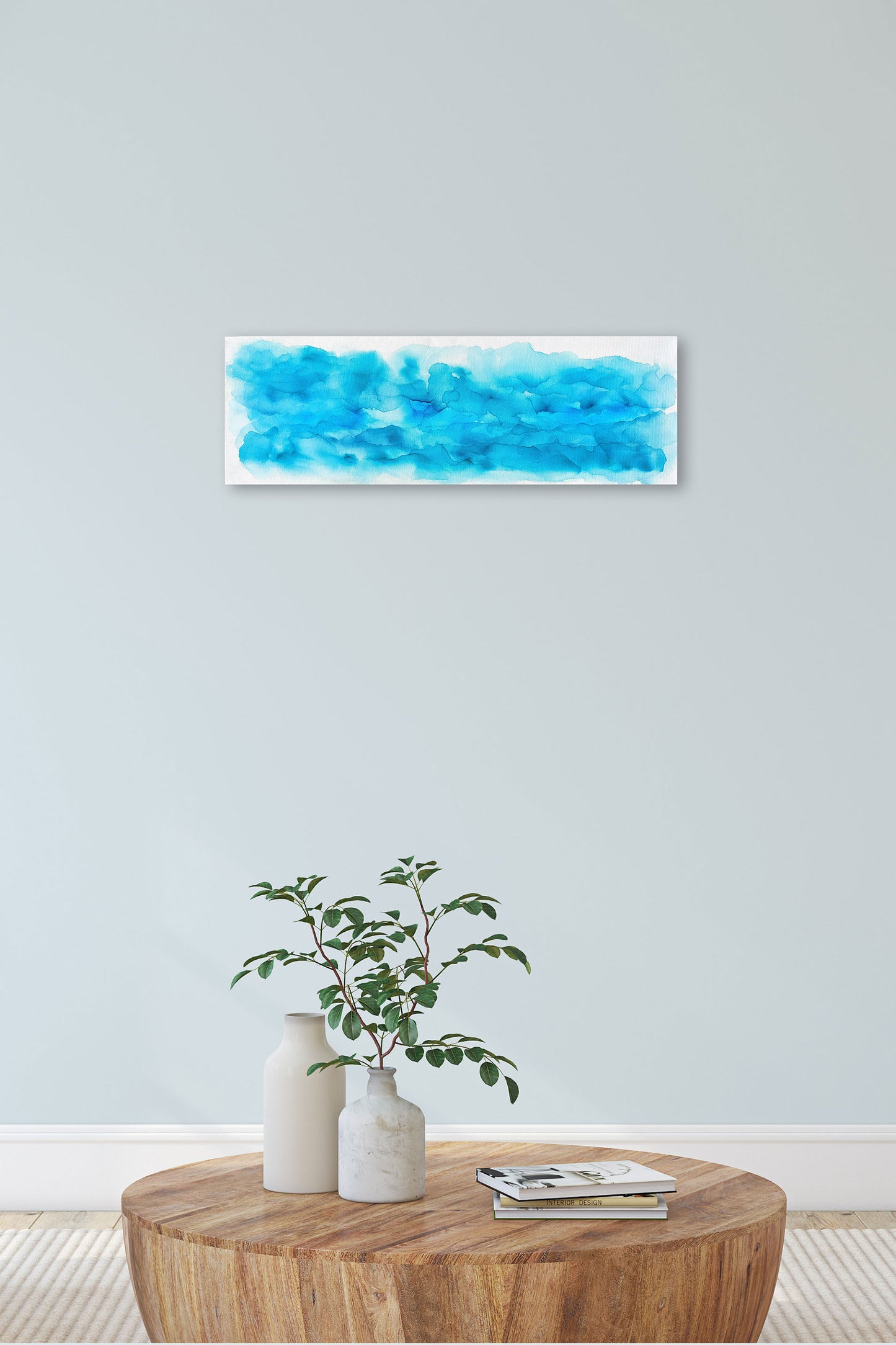 Digital mockup of Spoondrift hung on a pale blue wall in a living room. A wooden coffee table with ceramic vases, greens, and a stack of books is in the foreground.