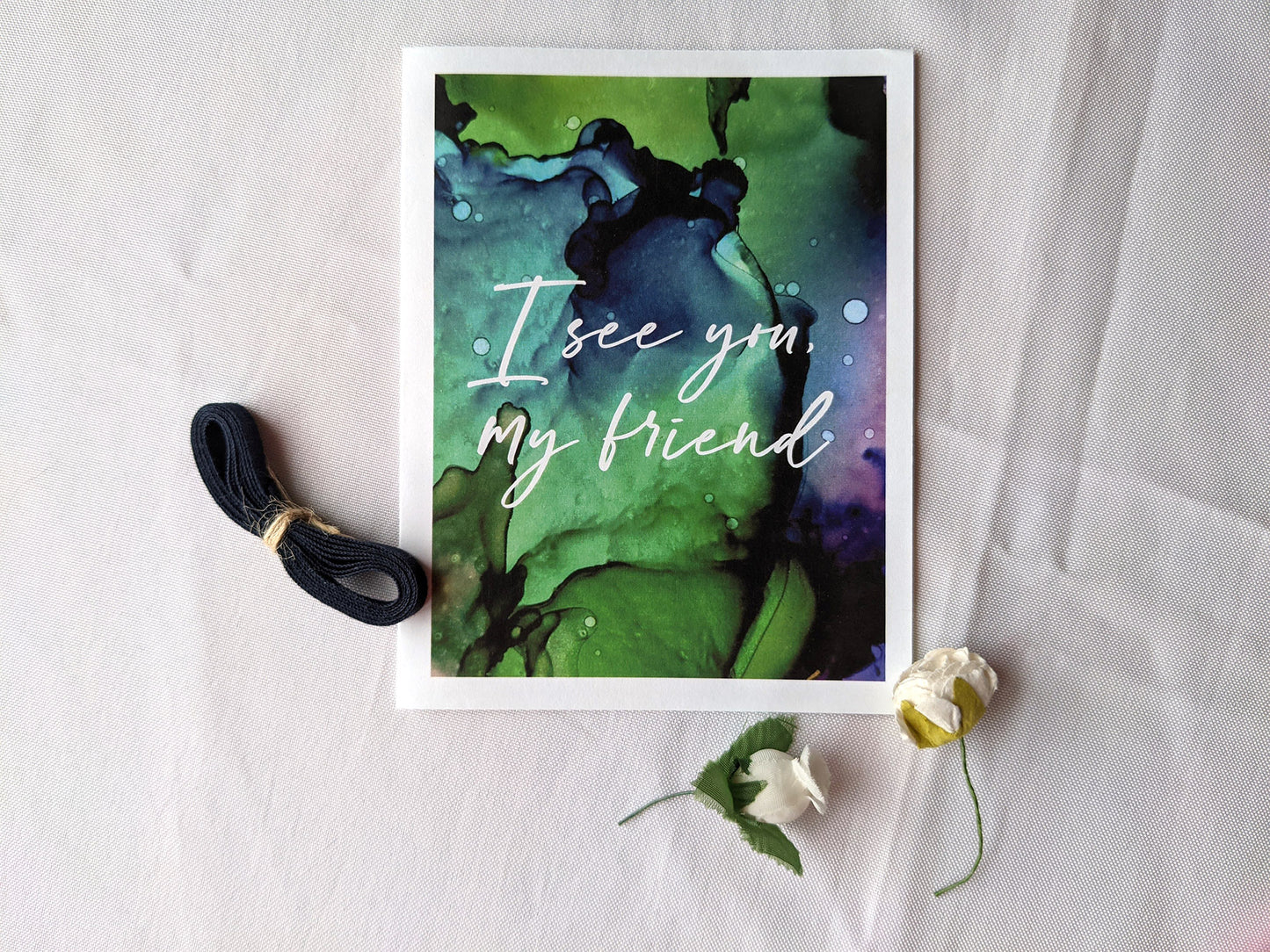 Greeting card on a white background with cotton ribbon and two faux flower buds.