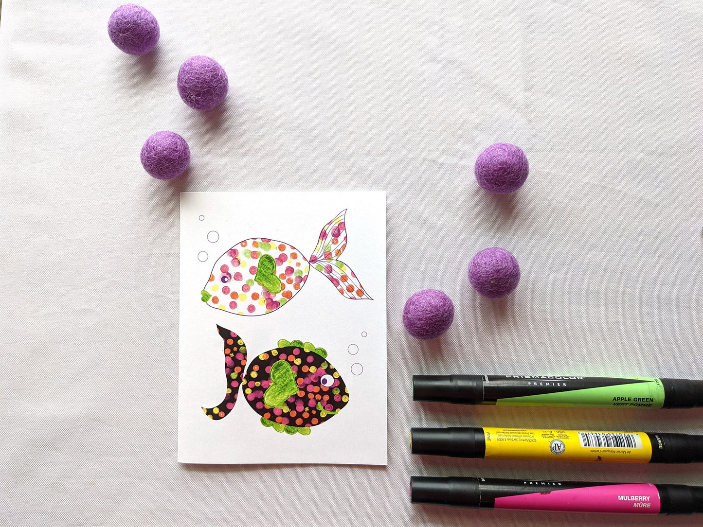 Greeting card laying on a white background with colorful felt balls and markers.
