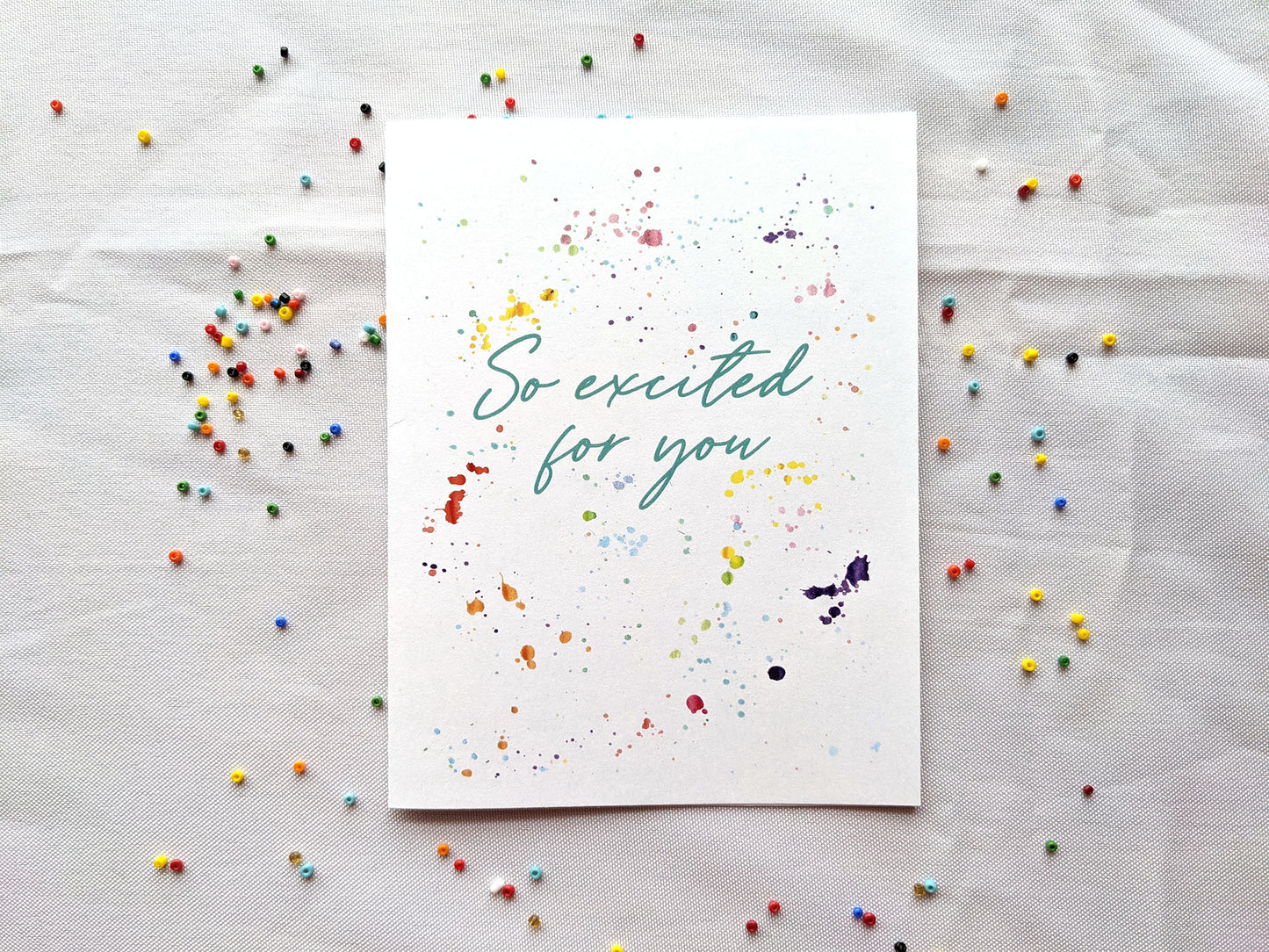 Greeting card laying flat on a white background with colorful seed beads surrounding it.