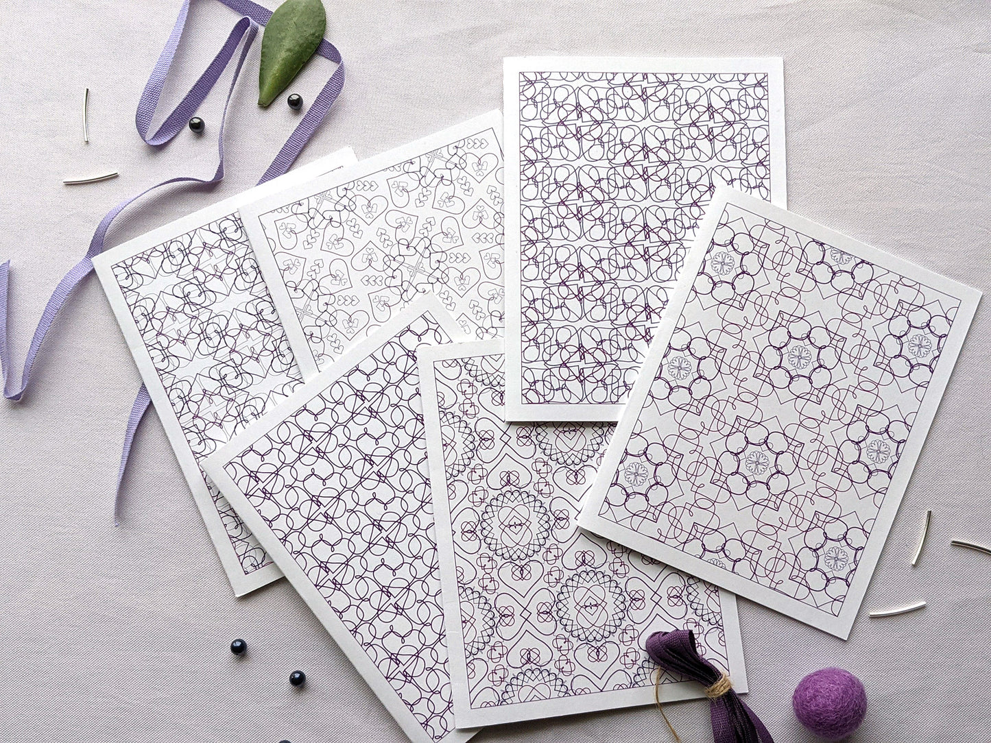 Six overlapping greeting cards on a white background with purple cotton ribbon, beads, and colorful felt balls.