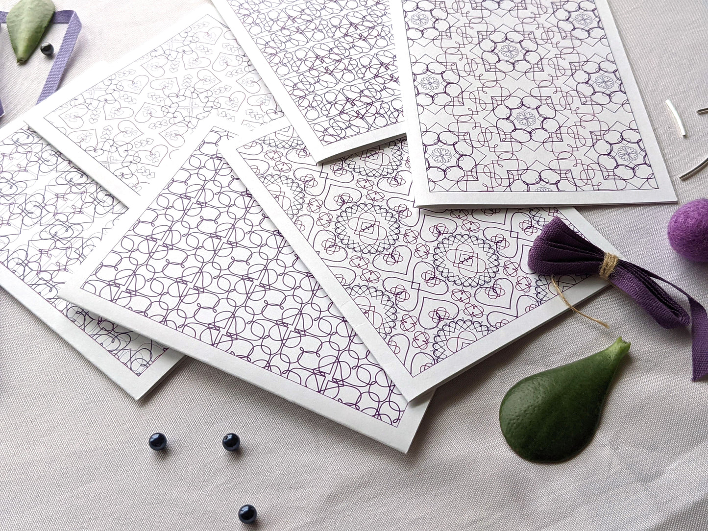 Angled view of six overlapping greeting cards on a white background with purple cotton ribbon, beads, and colorful felt balls.