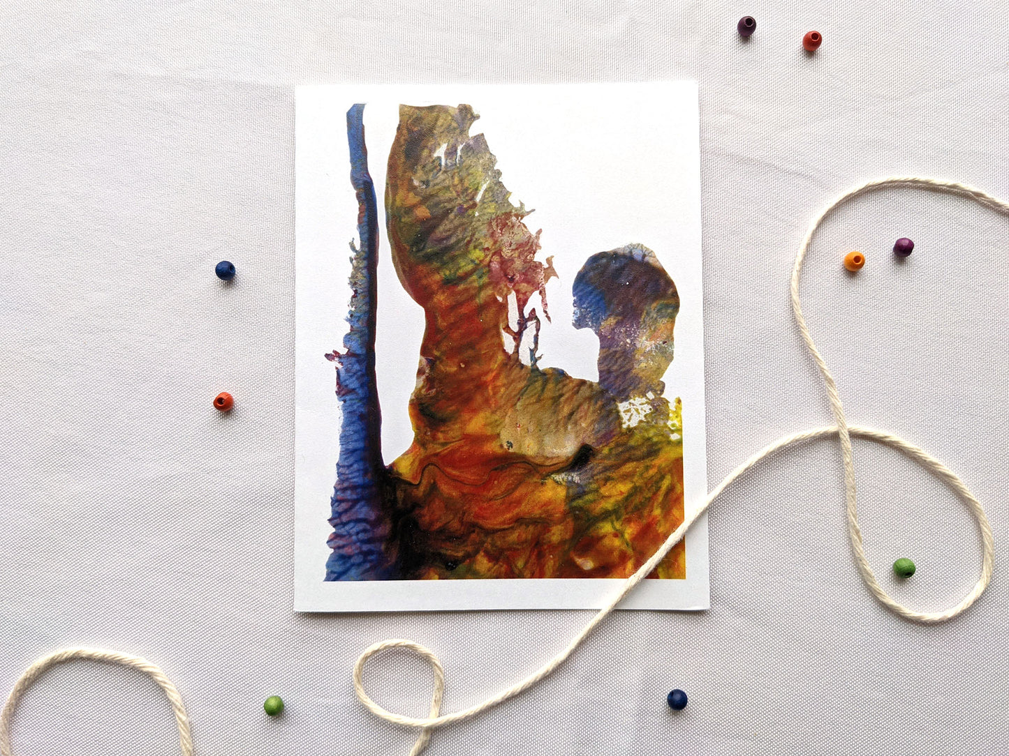 Greeting card laying on a white surface with colorful wooden beads and string.