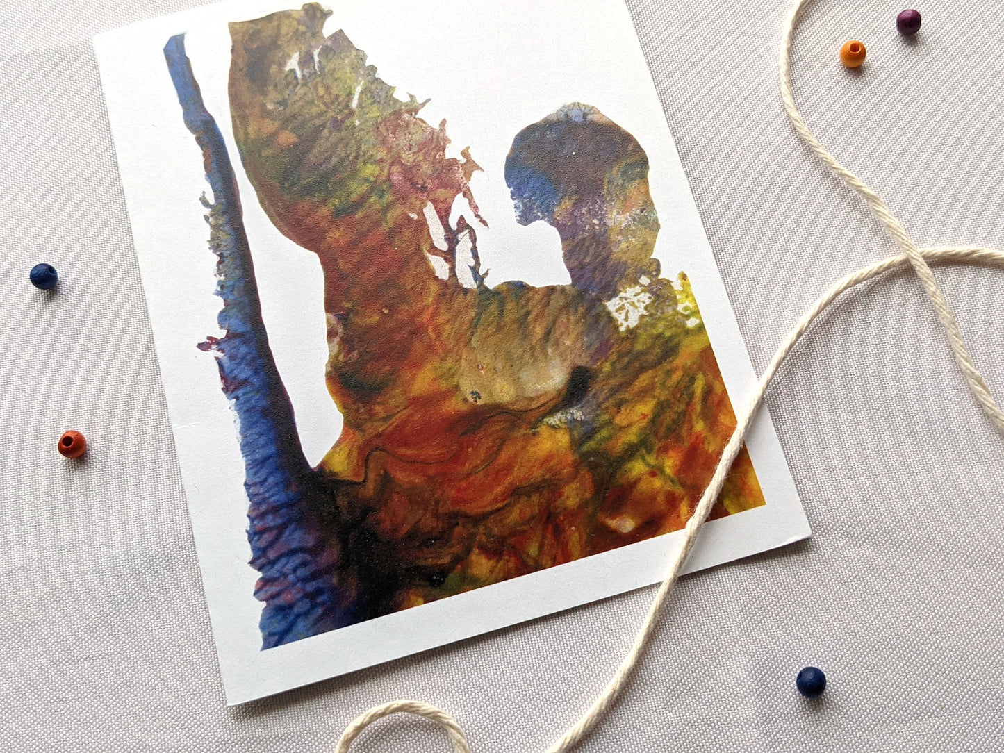 Angled view of greeting card on a white surface with colorful wooden beads and string.