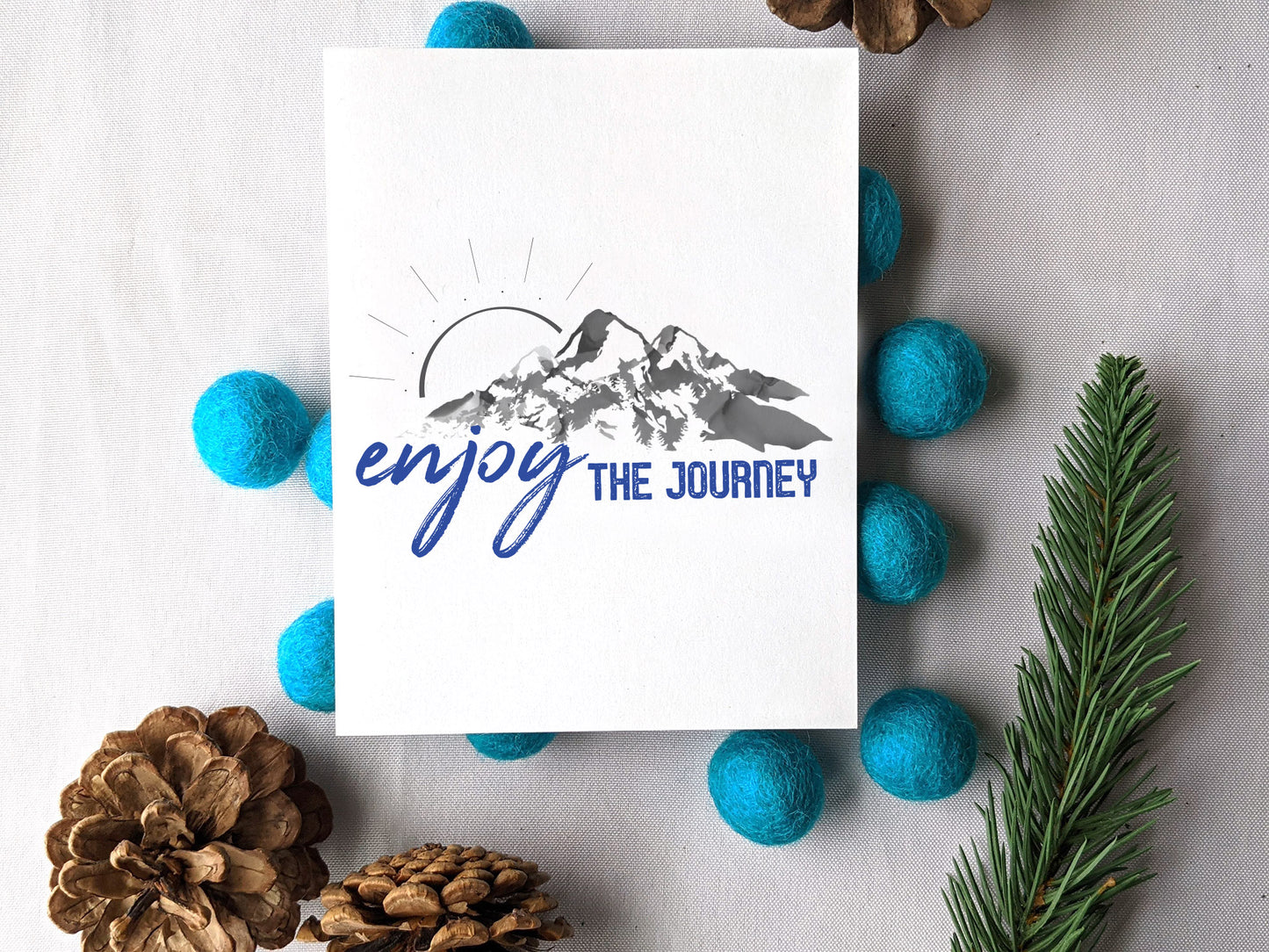 Greeting card on a pile of colorful felt balls with pinecones and an evergreen branch.