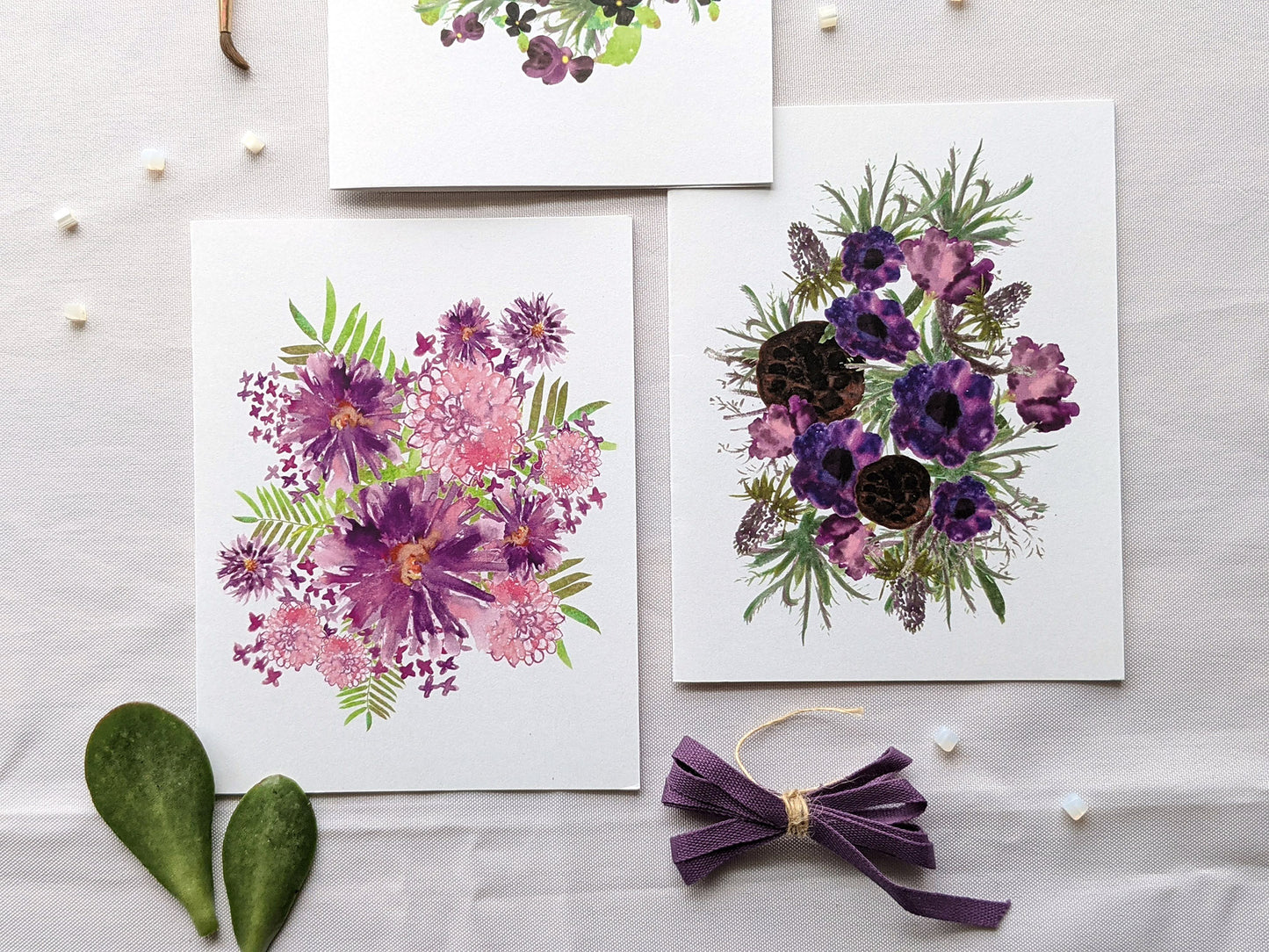 Greeting cards with colorful envelope laying on a white surface with green leaves and cotton ribbon wound on wooden spools.