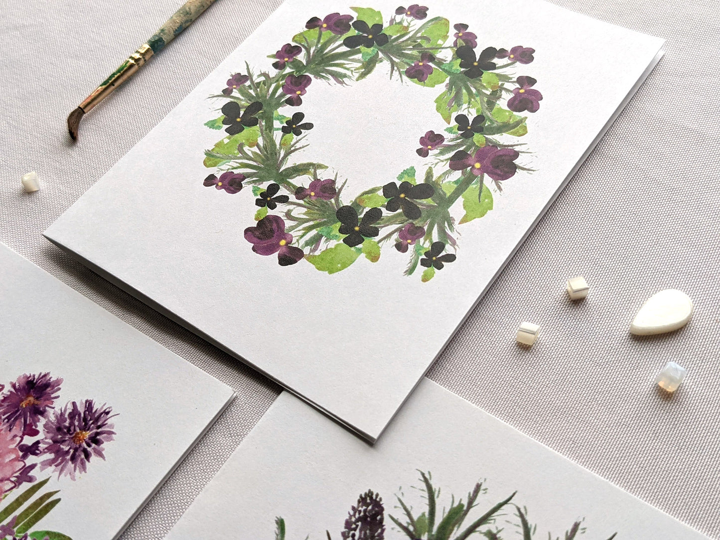 Angled view of greeting cards on a white surface with beads and paint brush.