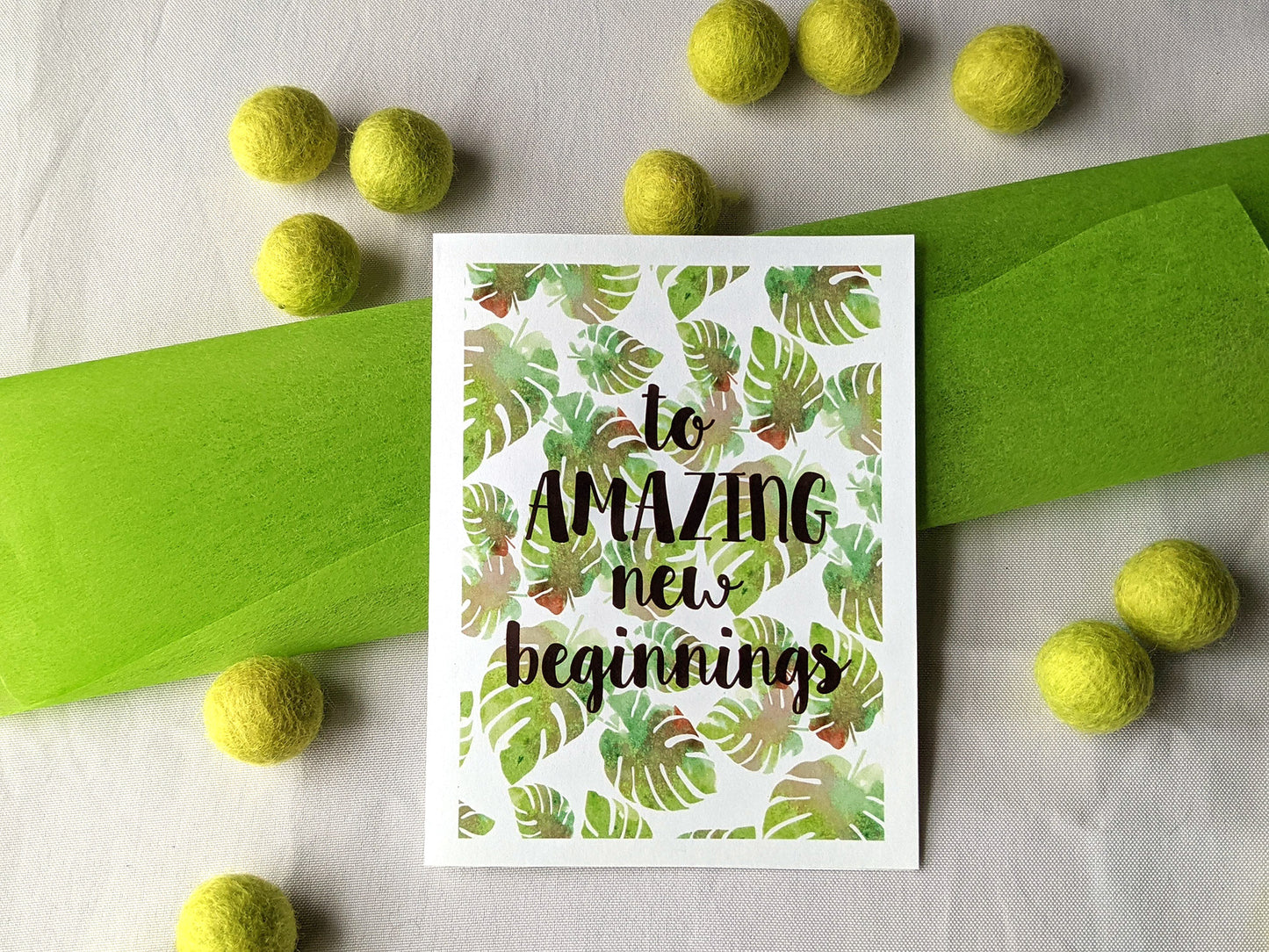 Greeting card laying with colorful envelope on white background with colorful fabric tissue and felt balls.