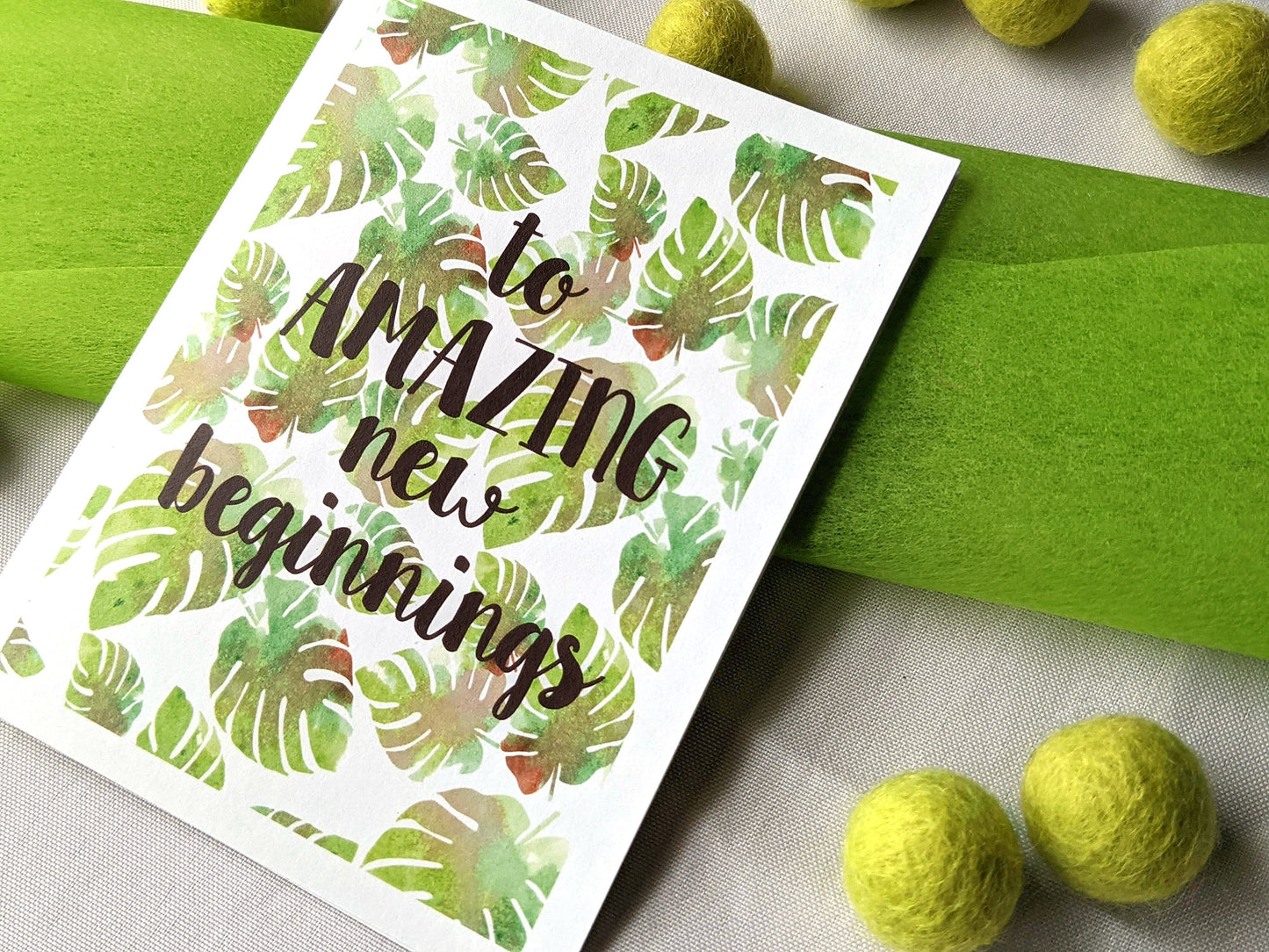 Angled view from above of greeting card laying with colorful envelope on white background with colorful fabric tissue and felt balls.
