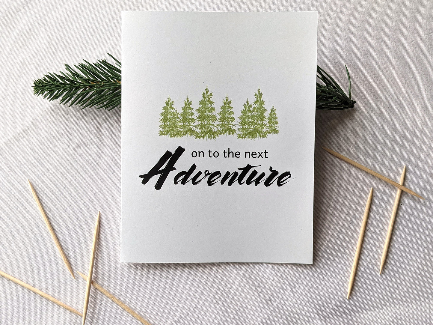 Greeting card on a white background with an evergreen branch and toothpicks.