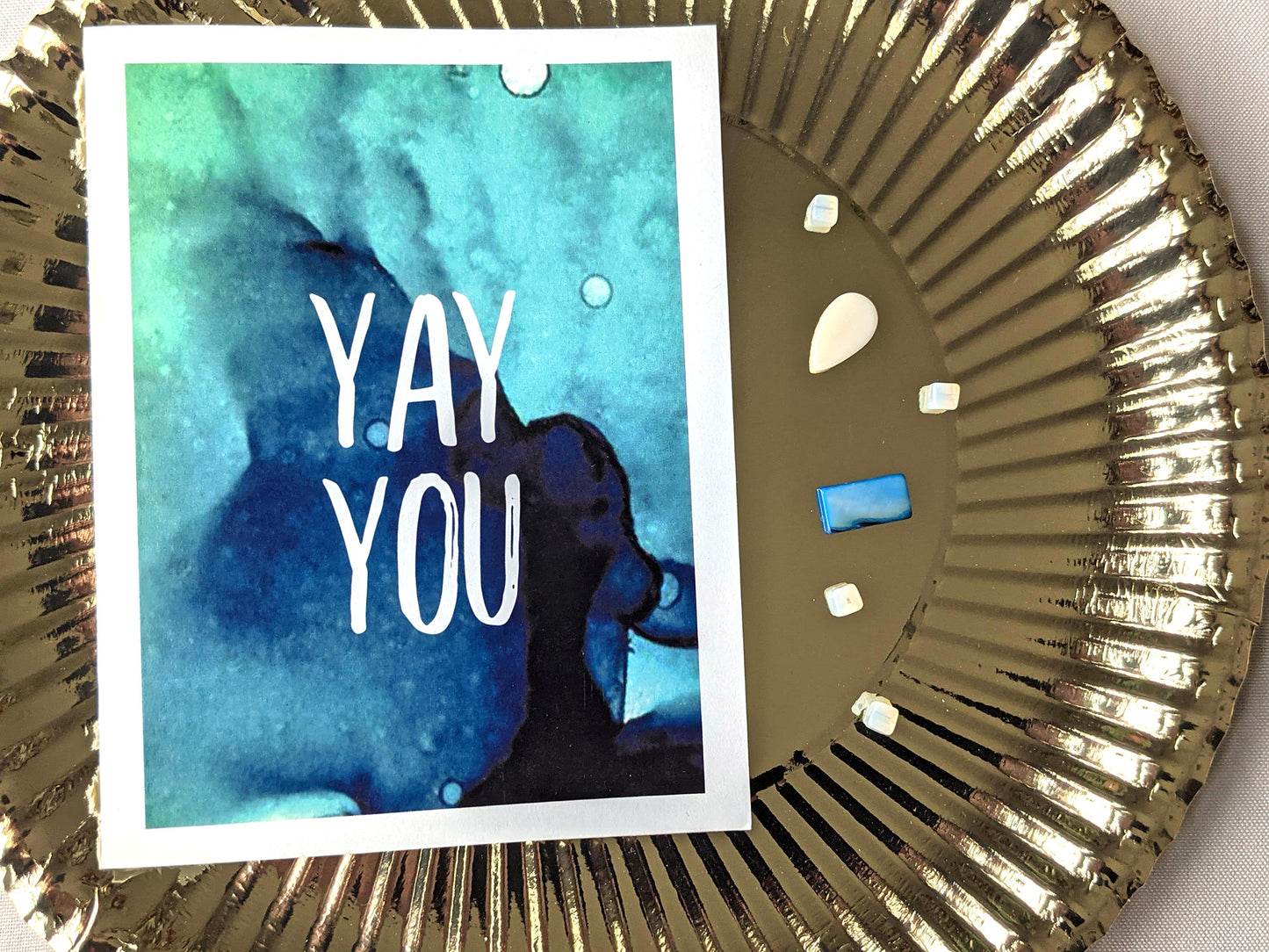 Greeting card laying on top of a gold party plate with beads sprinkled next to it.