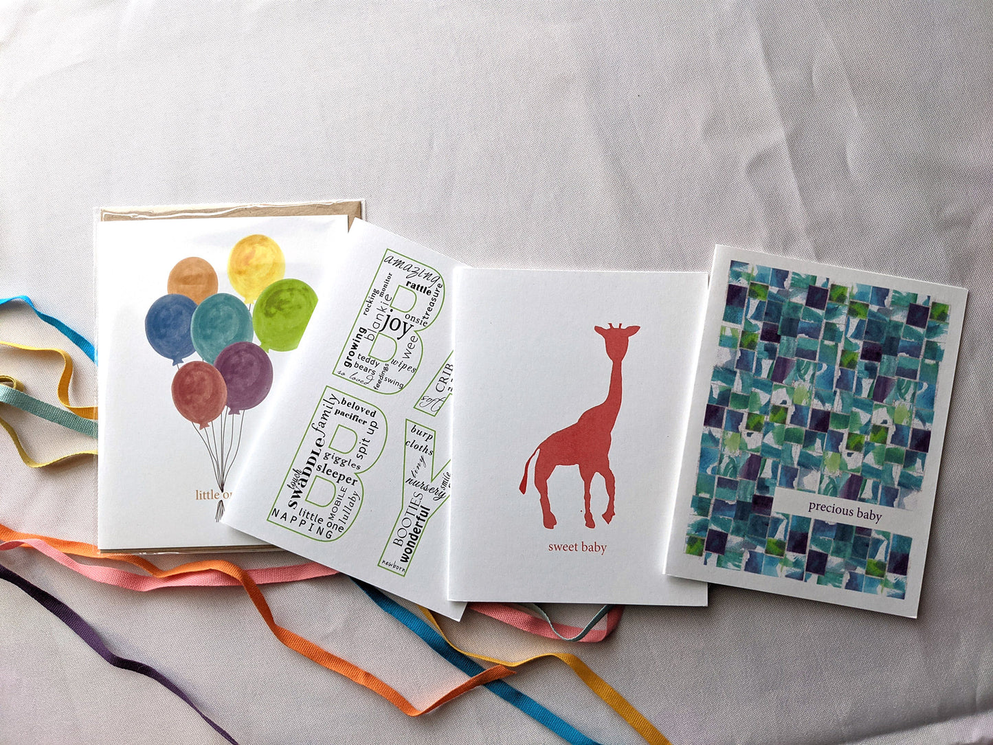 Four greeting cards overlapping on a white background with colorful cotton ribbons.