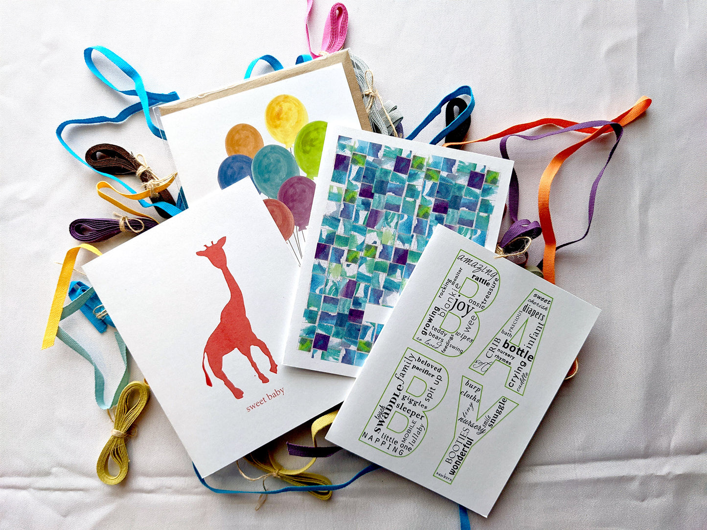 Four greeting cards overlapping on a white background with colorful cotton ribbons.