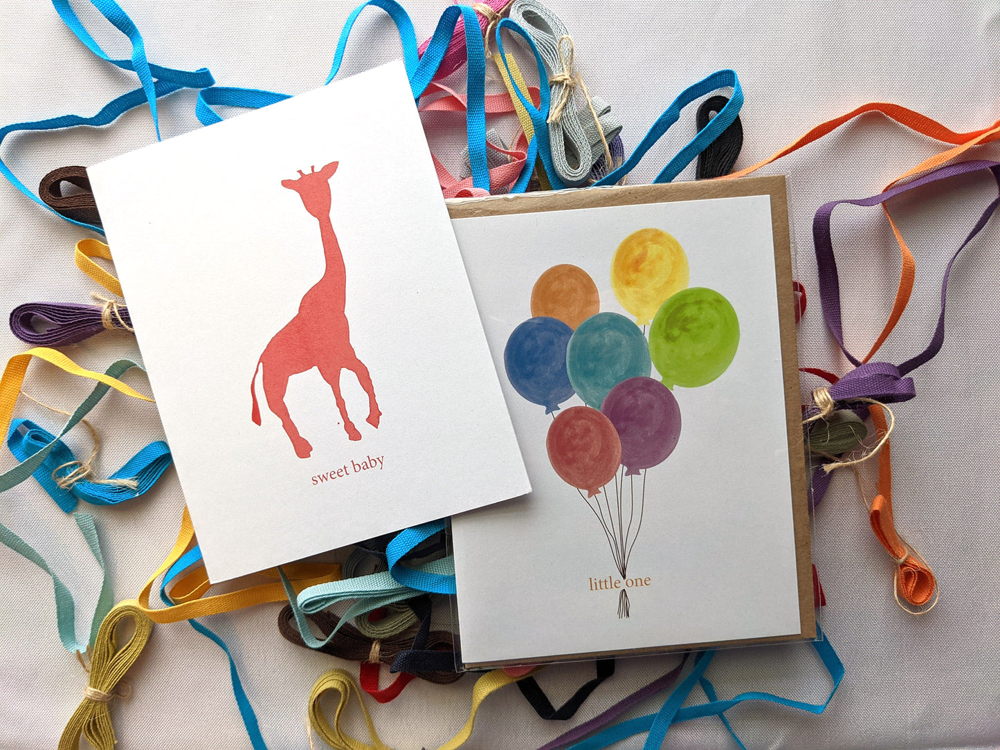 Two greeting cards overlapping on a white background with colorful cotton ribbons.
