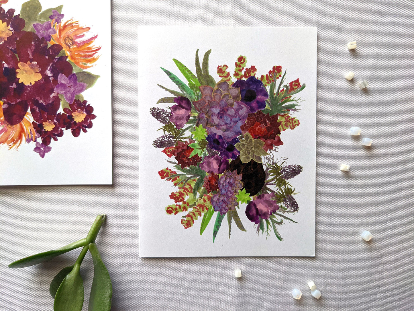 Greeting cards laying on a white surface with succulent leaves and beads.