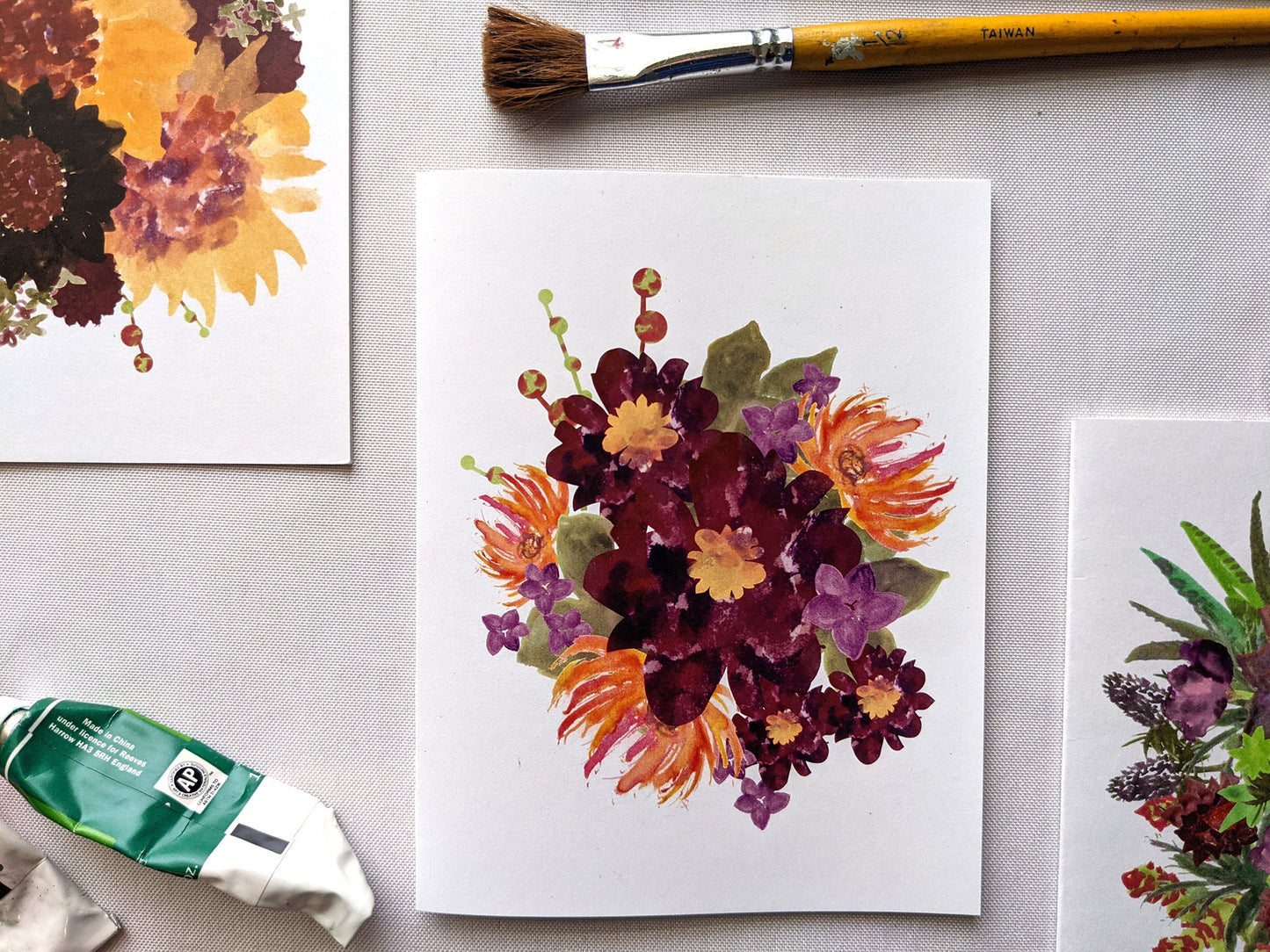 Greeting cards laying on a white surface with paint tubes and brushes.