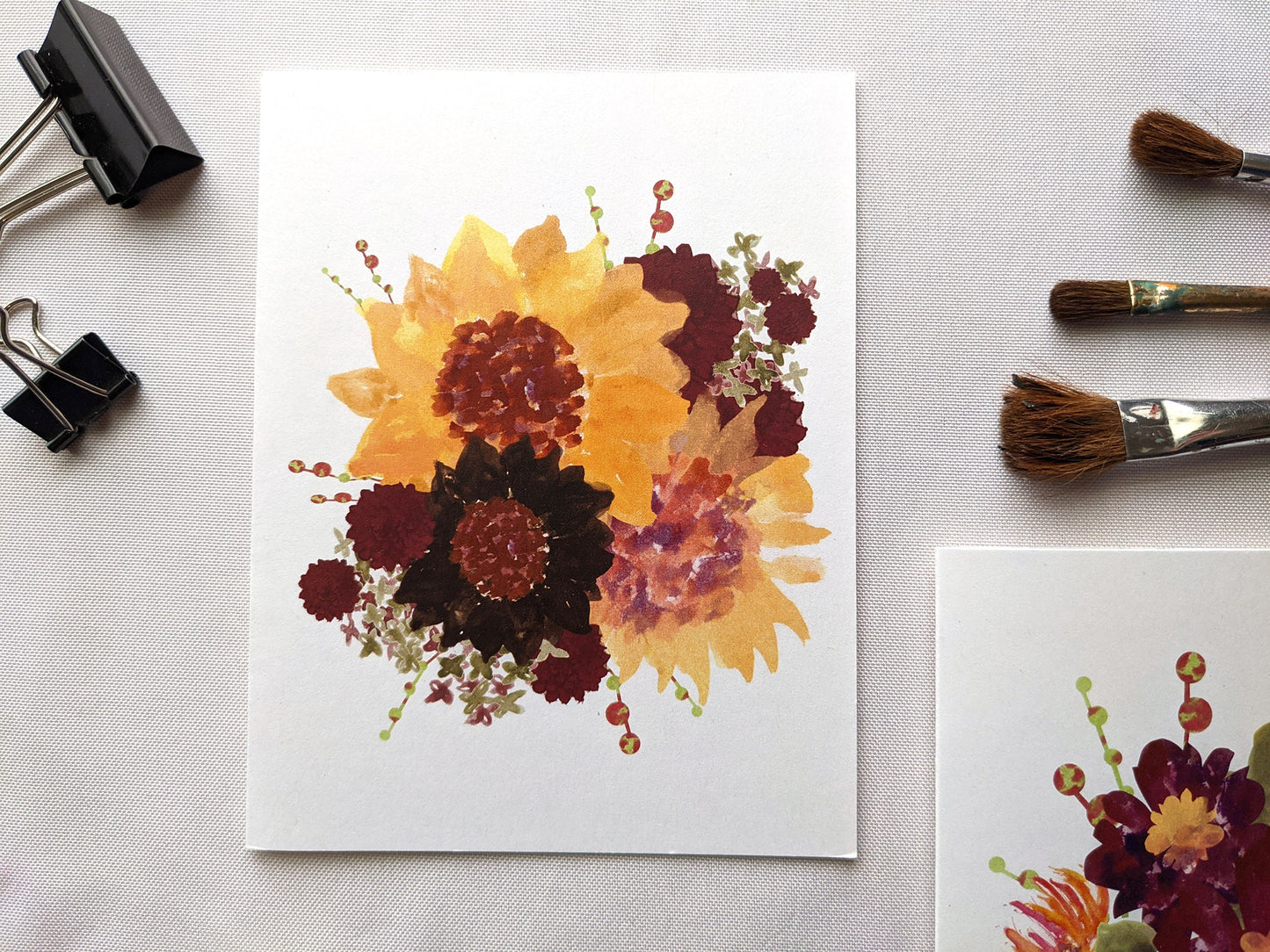 Greeting cards laying on a white surface with binder clips and paintbrushes.