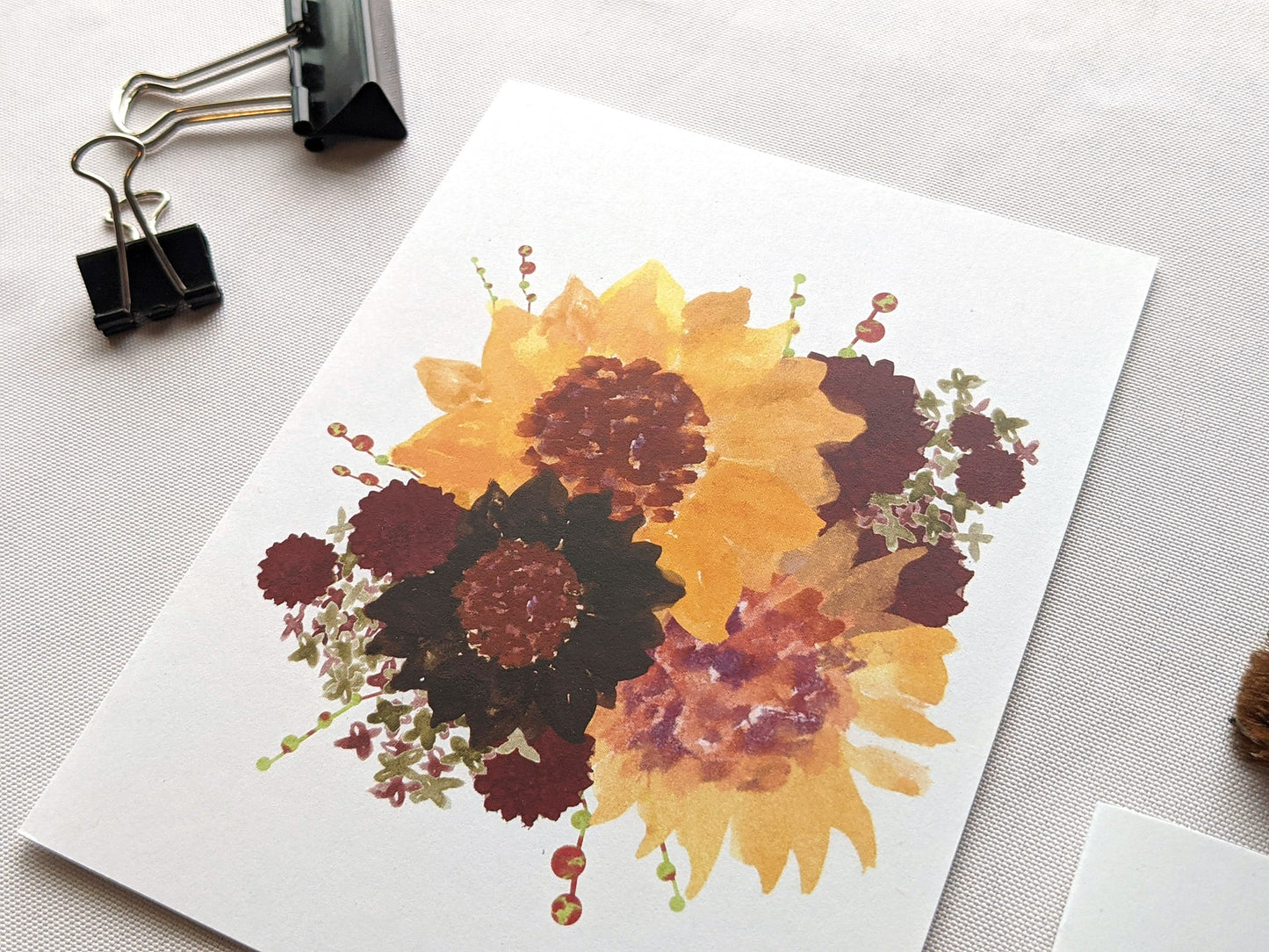 Greeting cards laying on a white surface with binder clips and paintbrushes.