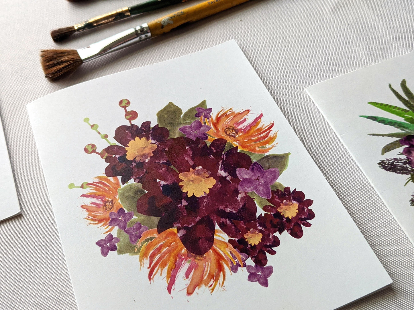 Angled view of greeting cards on a white surface with paint brushes.