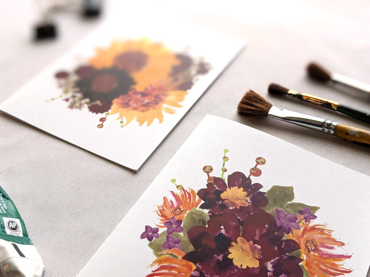 Angled view of greeting cards on a white surface with paint brushes.