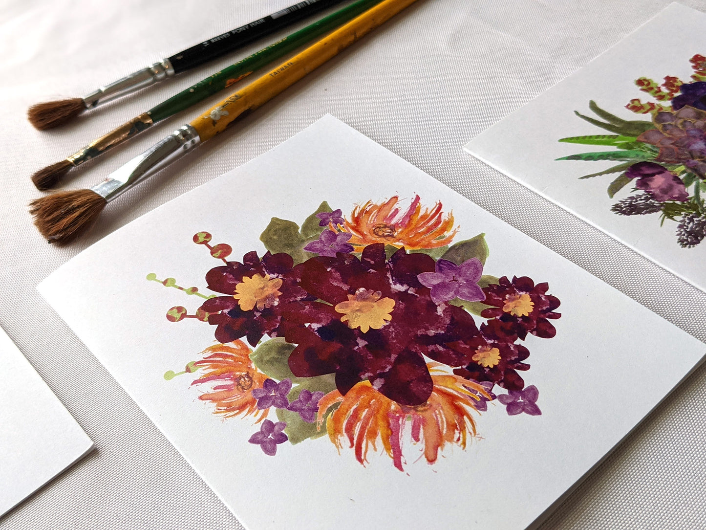 Angled view of greeting cards on a white surface with paint brushes.