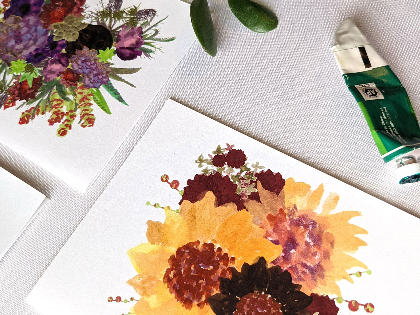 Angled view of greeting cards on a white surface with paint tubes.