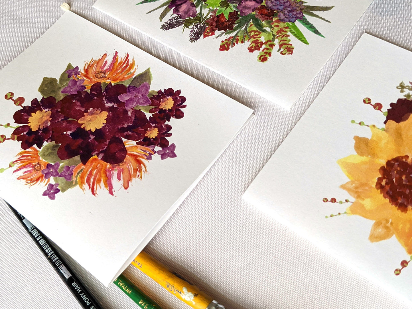 Angled view of greeting cards on a white surface with paint brushes.