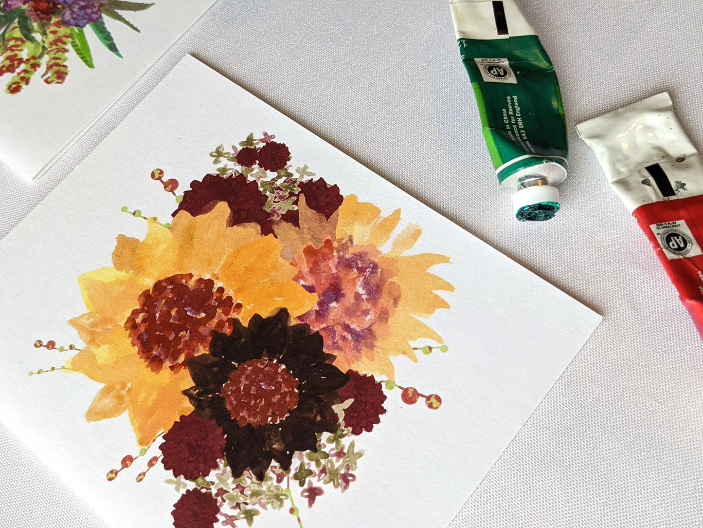 Angled view of greeting cards on a white surface with paint tubes.