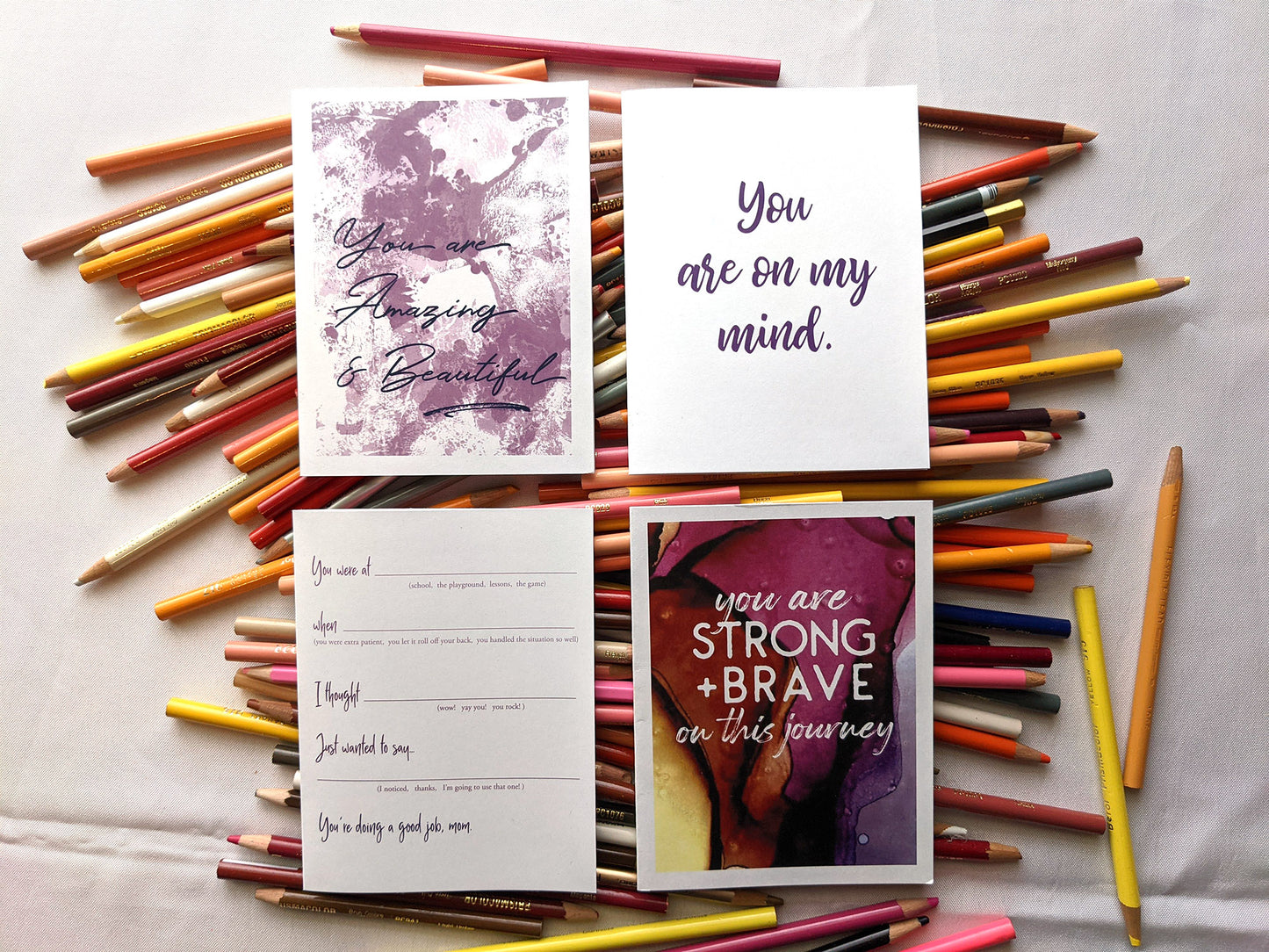 Four greeting cards laying on a pile of colored pencils.