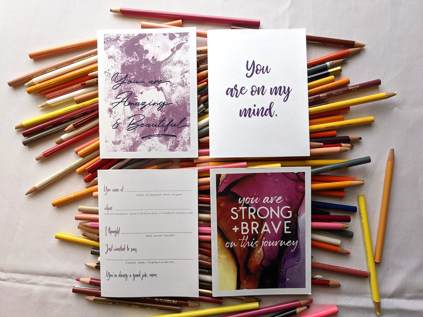 Four greeting cards laying on a pile of colored pencils.