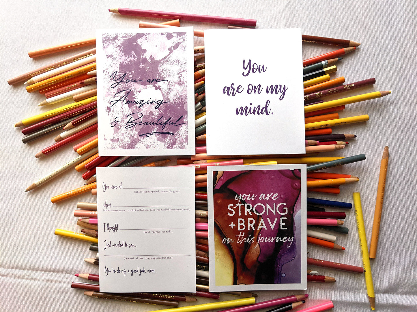 Four greeting cards laying on a pile of colored pencils.