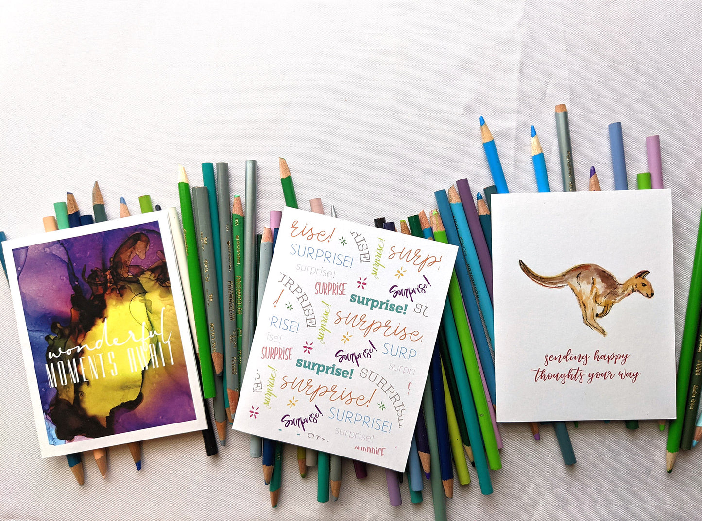 Three greeting card laying on a pile of colored pencils.