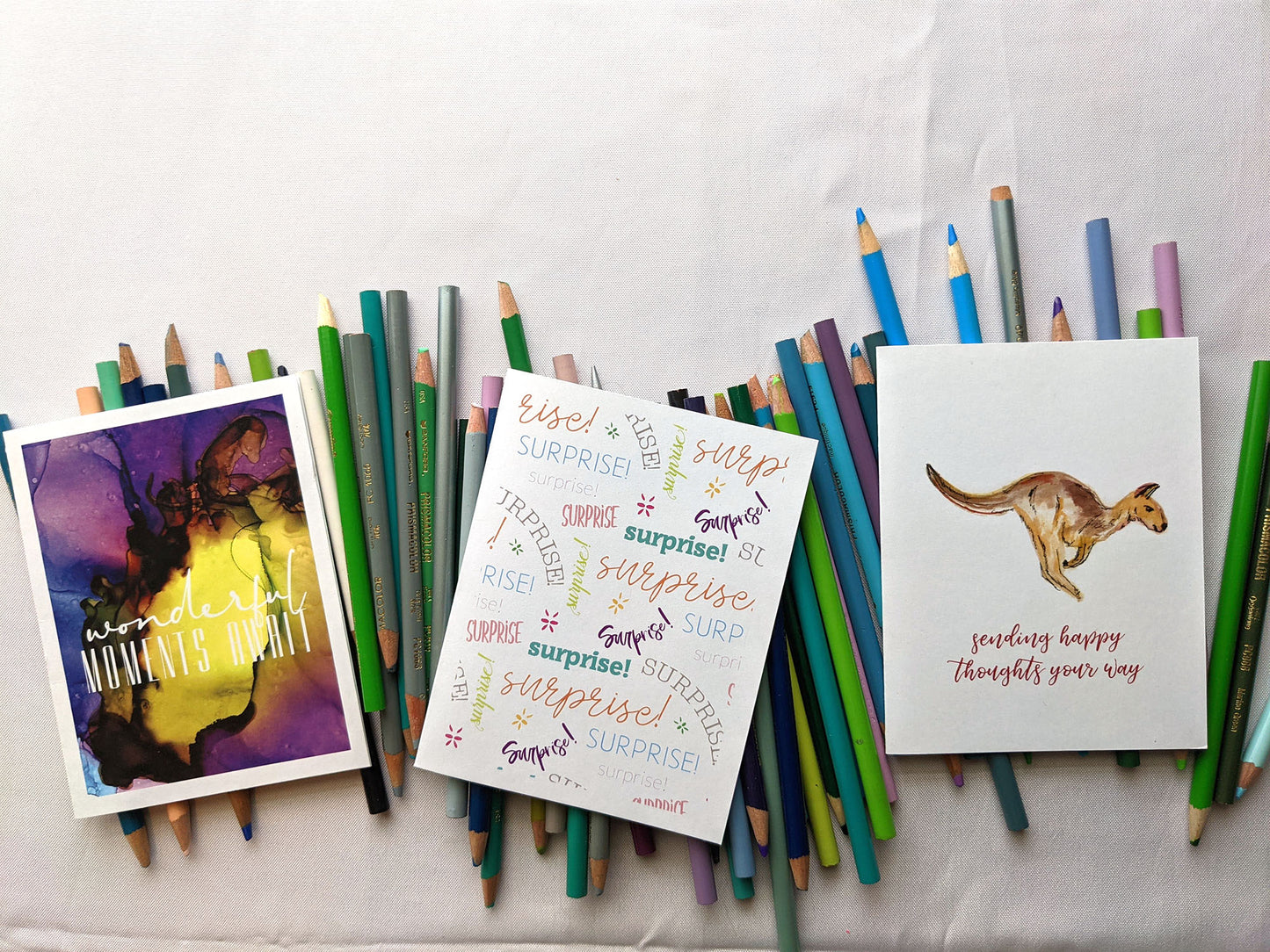 Zoomed out view of three greeting cards laying on a pile of colored pencils.