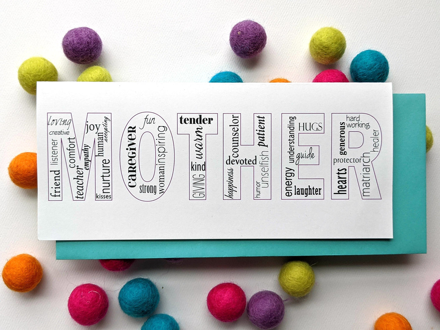Greeting card with colorful envelope laying on a pile of colorful felt balls.