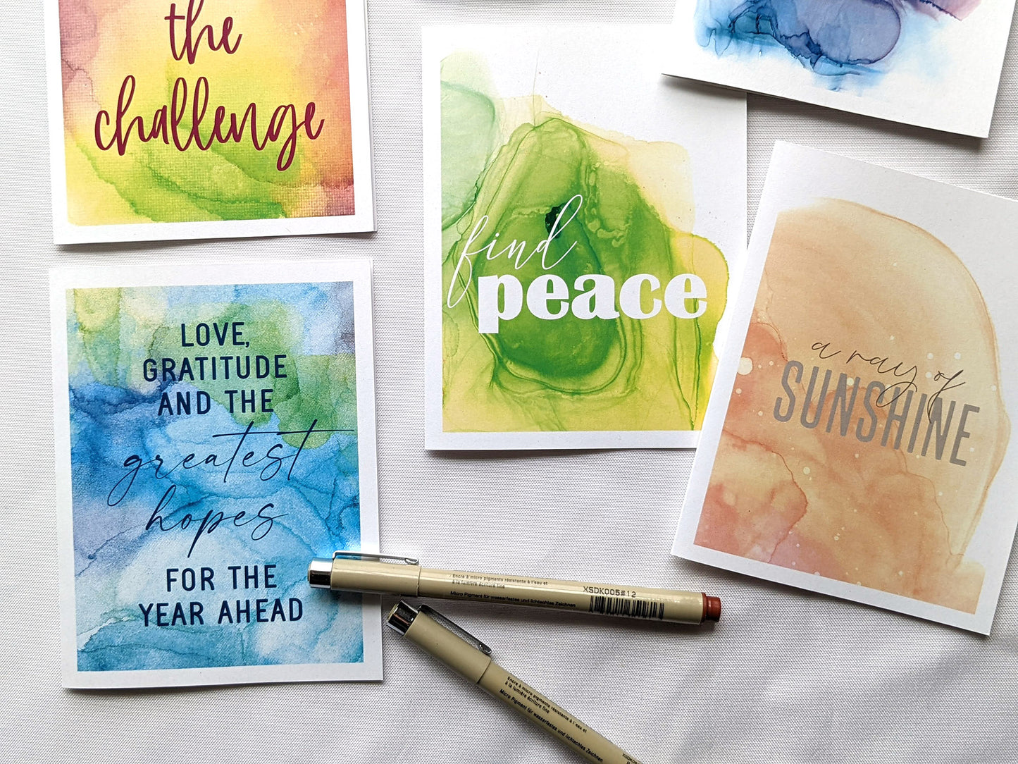 5 greeting cards laying on a white background with micron pens.