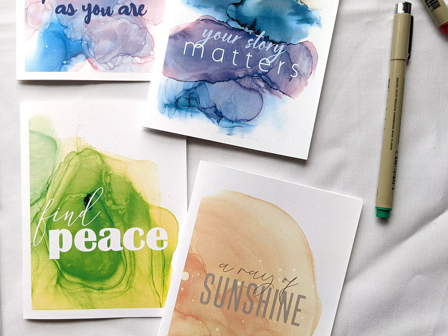 4 greeting cards laying on a white background with micron pens.