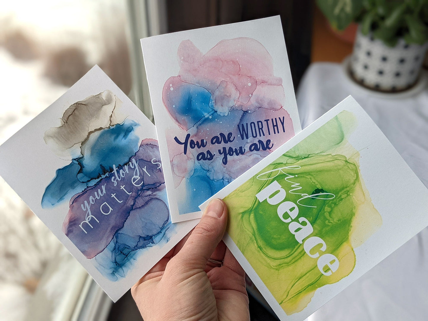 Hand holding three greeting cards fanned out near a window.