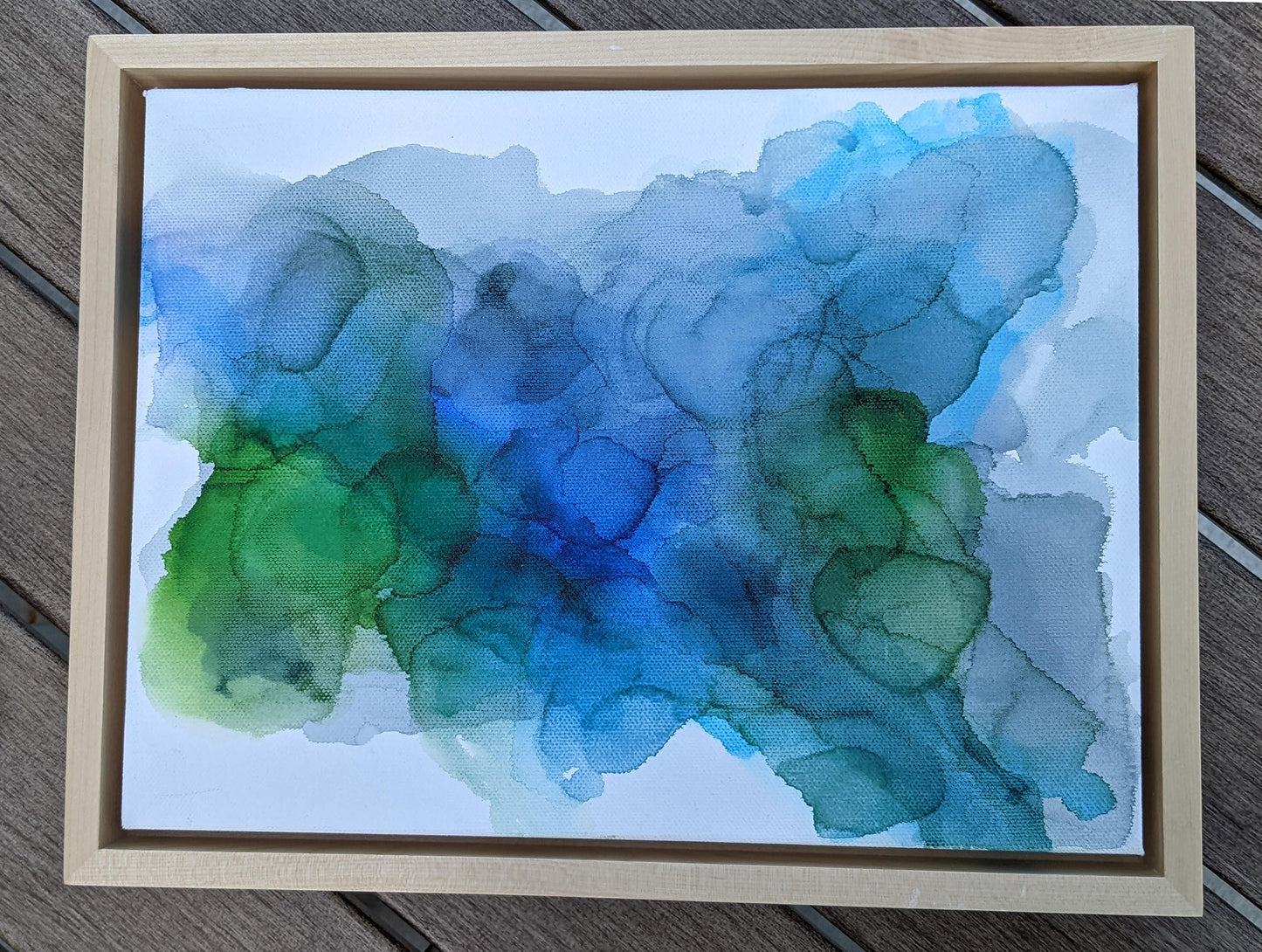 Photo from above of the canvas in a light maple float frame laying on a slat patio table.
