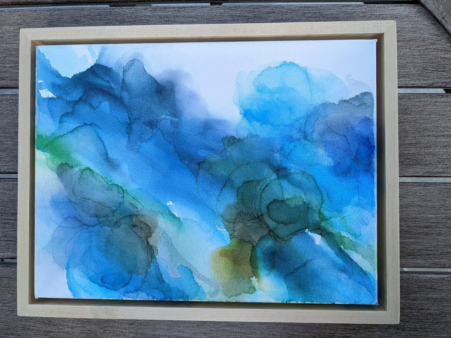 Photo from above of the canvas in a light maple float frame laying on a slat patio table.