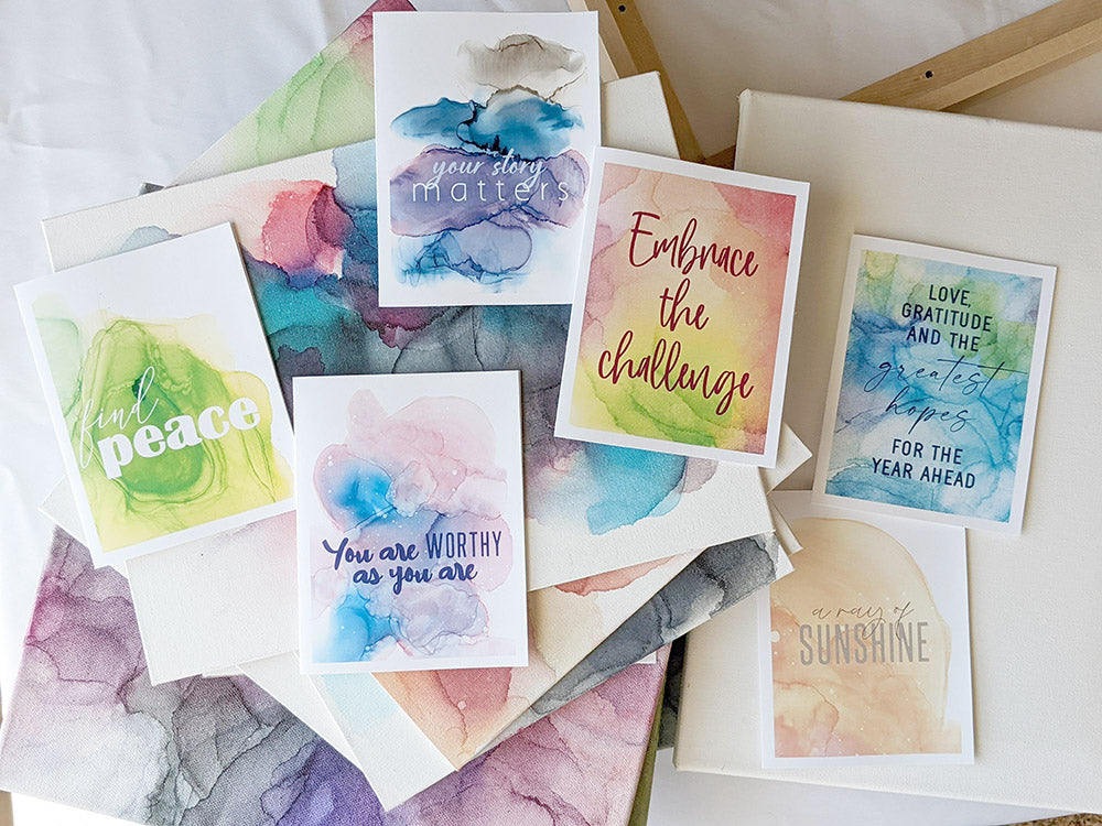 6 greeting cards arranged on top of a stack of the canvases from the original alcohol ink paintings.